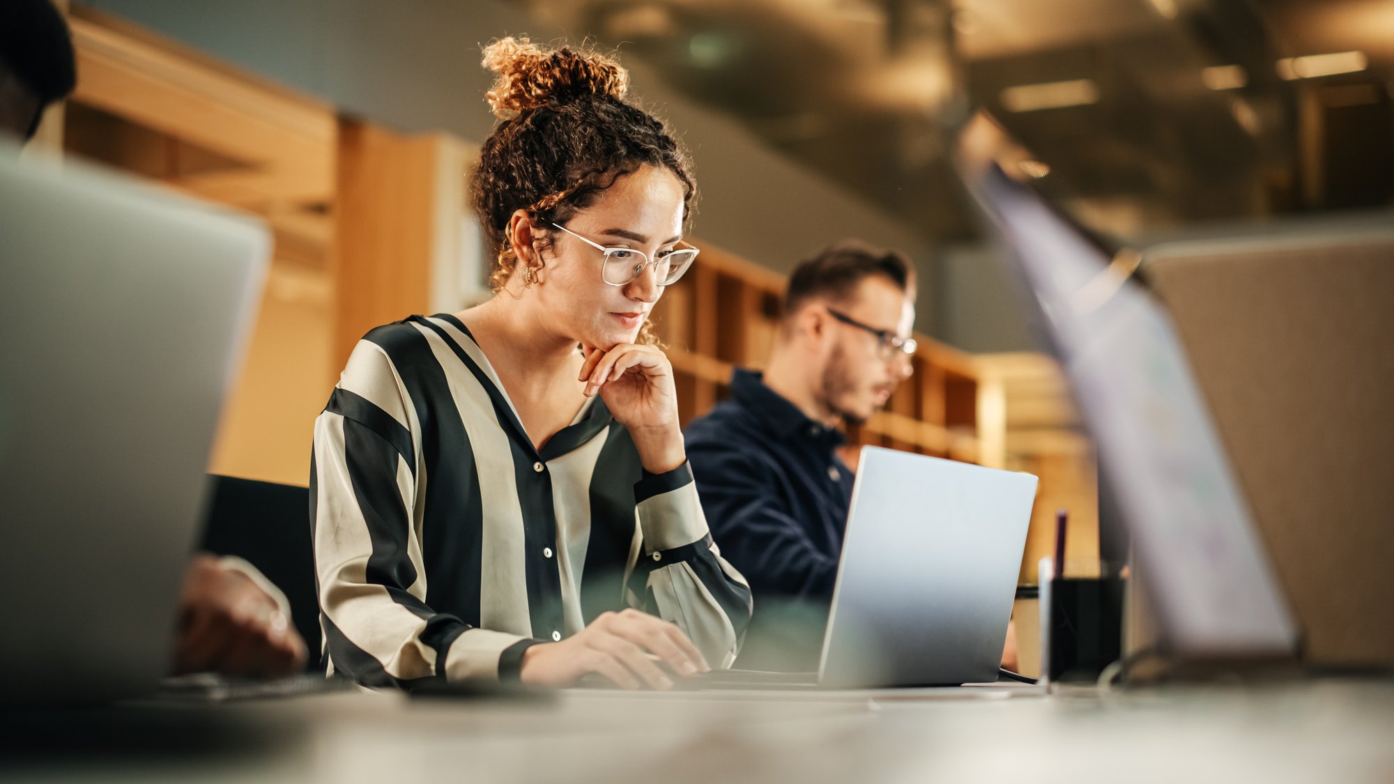 Woman working on a laptop alongside colleagues in a modern creative studio.