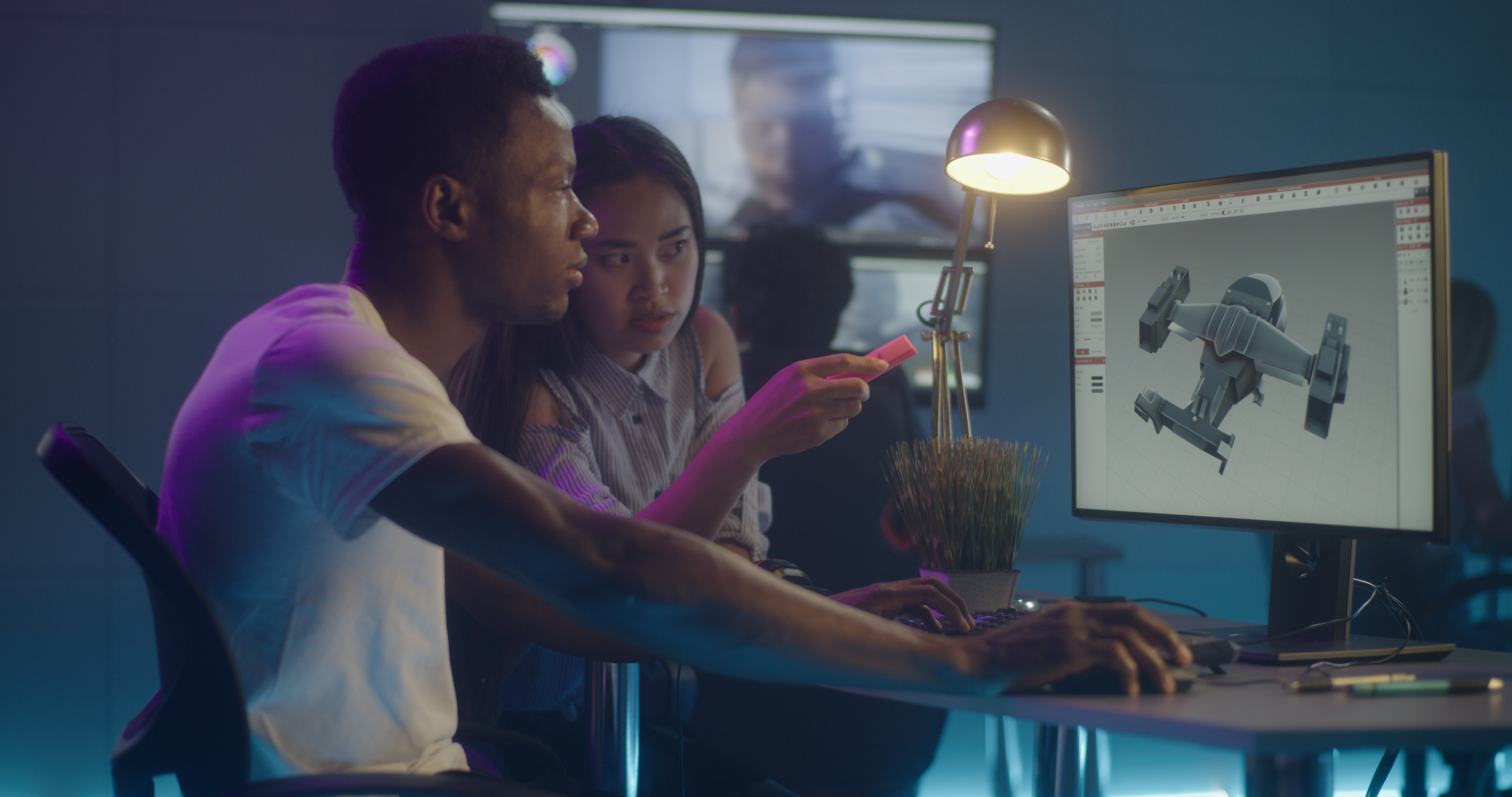 Workers in a creative studio, both are looking at a computer monitor and 3D modelling software